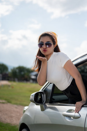 A playful and cheerful Asian woman in sunglasses is enjoying the wind outside the car and having fun...
