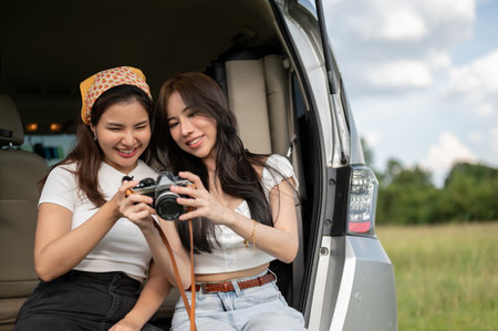 Two happy Asian female best friends are checking the pictures on the camera together, enjoying...