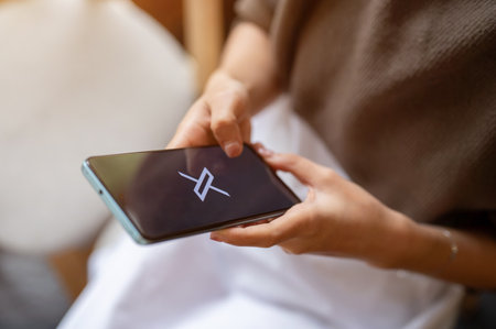 Chiang mai, Thailand - Oct 12 2023: A woman is using X Twitter on her smartphone while relaxing in a cafe. X Twitter logo on an iPhone 14. Social media platform conceptのeditorial素材