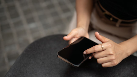 Close-up image of a trendy Asian woman using her smartphone while relaxing in a cafe in the city....