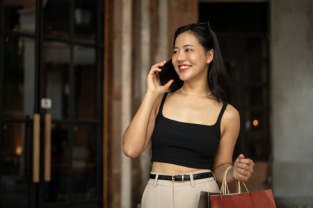 A trendy young Asian woman is talking on the phone with her friend during her shopping day in the city. Shopping spree, Urban lifestyle, City girlの写真素材