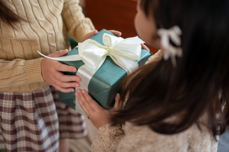 Close-up image of a young girl giving a Christmas gift to her friend or sister. Merry Christmas,...