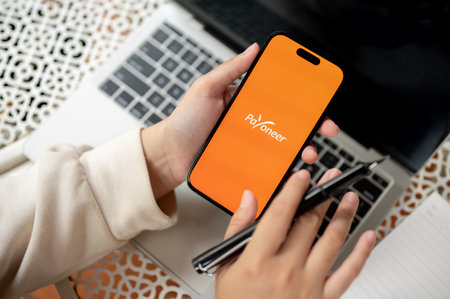 Chiang Mai, Thailand - Oct 19 2023: close-up image of a woman using a Payoneer application on her Iphone14 at her modern office desk. Payoneer logo on Iphone14 screenのeditorial素材