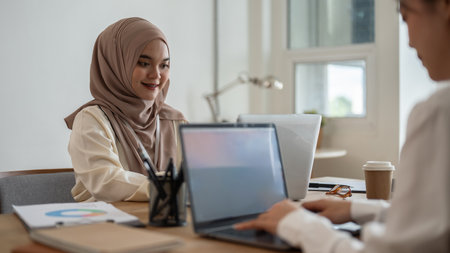 A beautiful millennial Asian-Muslim businesswoman working on a project with her colleague in the office. Businesspeople conceptの写真素材