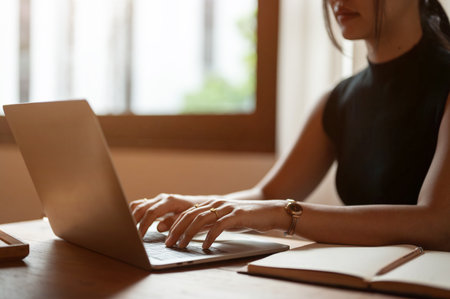 Cropped image of a beautiful Asian woman working on her laptop, typing on the keyboard, responding to emails, or searching for information on the internet while sitting at a table in a coffee shop.の写真素材