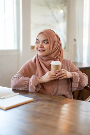 A portrait of a beautiful and relaxed Asian-Muslim woman wearing a hijab is looking away from the...