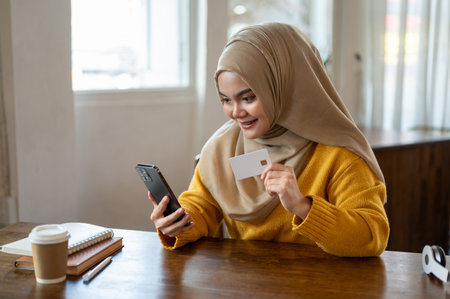 An attractive Asian-Muslim woman wearing a hijab is using a mobile banking application to pay her...