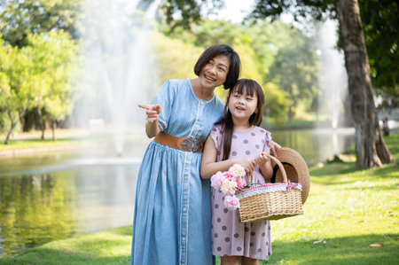 A happy and kind Asian grandmother is walking and having fun in the green park with her lovely granddaughter on the weekend. Leisure and family bonding conceptの写真素材