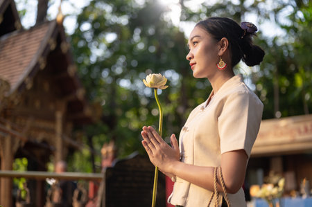 Side view image of a beautiful Asian woman in a traditional Thai-Lanna dress with a lotus flower in her hands is making a wish in a temple. praying, paying respect to the Buddha, Thai cultureの写真素材