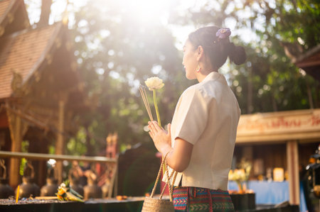 A beautiful Asian Thai woman in a traditional Thai-Lanna dress is making a wish and paying respect to the image of the Buddha at a temple. Thai culture, Buddhistの写真素材