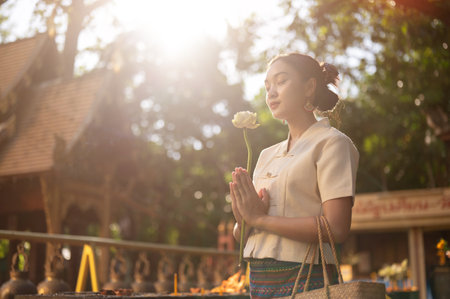 Side view image of a beautiful Asian woman in a traditional Thai-Lanna dress with a lotus flower in her hands is making a wish in a temple. praying, paying respect to the Buddha, Thai cultureの写真素材