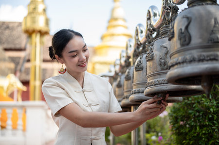 A beautiful Thai-Asian woman in a traditional Thai-Northern dress is ringing temple bells in a temple, making a wish and making a merit on a Buddhist holy day. Thai-culture, Buddhistの写真素材