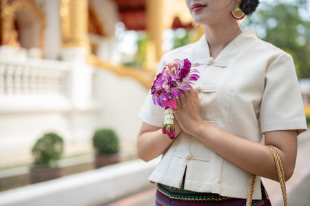 A beautiful young Thai-Asian woman in a traditional Thai-Northern dress is standing in a temple in a prayer position with a garland in her hands. pay respect, make a merit, make a wish, cropped imageの写真素材