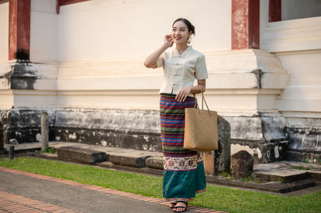 A portrait of a beautiful young Thai-Asian woman in a traditional Thai-Northern dress is in a beautiful temple. Thai culture, Buddhism, cultural travel, and lifestyle, full body pictureの写真素材