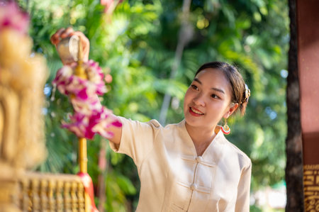 A charming Asian woman in a traditional Thai-Lanna dress is making a libation, making a merit at a temple on a Buddhist holy day. Thai culture, Buddhist, make a wishの写真素材