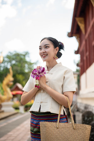 A beautiful young Thai-Asian woman in a traditional Thai-Northern dress is standing in a temple in a prayer position with a garland in her hands. pay respect, make a merit, make a wish, Buddhismの写真素材