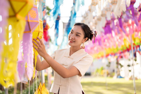 A beautiful and happy Thai-Asian woman in traditional dress is hanging a paper lantern and enjoying YI Peng or Loy Krathong festival at a temple in Chiang mai. Thai-Lanna culture, Thai festivalの写真素材