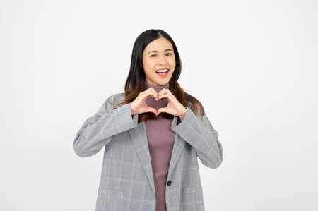 Beautiful smiling Asian businesswoman making heart shape hand sign on white isolated background.の写真素材