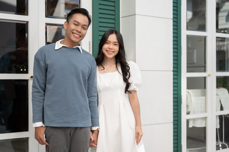 Young beautiful Asian couple standing in front of their house, having a good time together. Couple concept.の写真素材