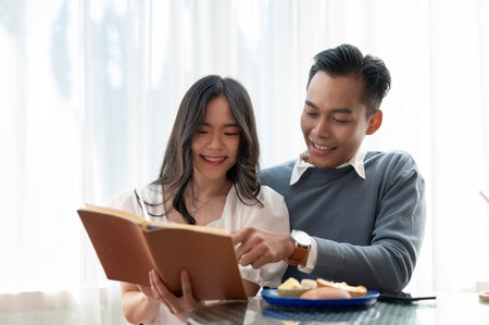 Young beautiful adorable Asian couple sharing their free time together, reading books in a cute cafe. Couple concept.の写真素材