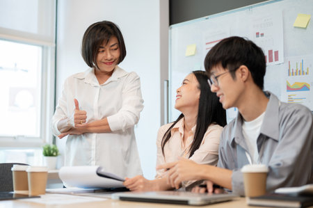 A satisfied and happy senior female boss is giving a thumb up to her team during the meeting. A boss feels satisfied with a project outcome and gives a compliment to her colleagues.の写真素材