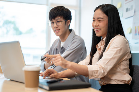 Two happy young Asian male and female colleagues are working on a project on a laptop in the office together.の写真素材