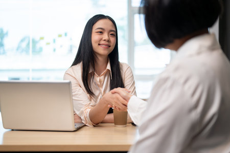 A beautiful and friendly young Asian businesswoman is shaking her hand with a senior female client...