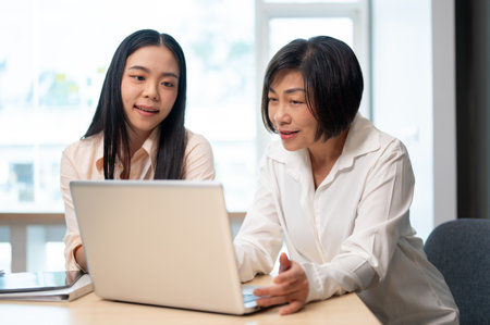 A young businesswoman and senior female boss are sharing their ideas and working on a project on a laptop computer in the meeting room together.の写真素材