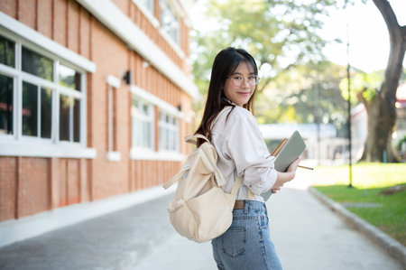 Young beautiful Asian female college student in casual clothes with a backpack and laptop computer is in a campus.の写真素材
