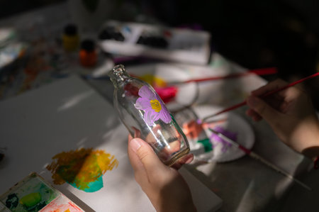 Close-up image of a man painting on a glass bottle, handcrafting home decoration, joining an art workshop. art workshop, creative activity, reuseの写真素材
