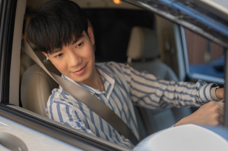 A happy and handsome young adult Asian man in casual outfit is driving a car, looking at the side-view mirror.の写真素材