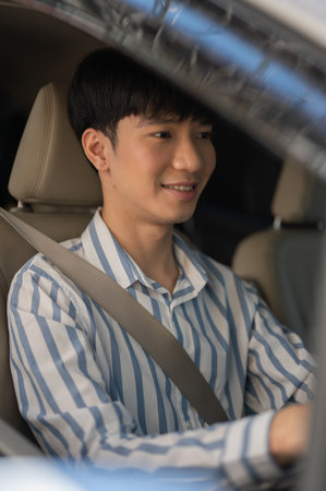 A handsome, happy young adult young Asian man in casual outfit is driving a car with a seatbelt on. People and vehicle conceptsの写真素材