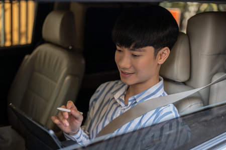 A happy and busy Asian man or businessman is using his digital tablet in his car, working in his car. People and vehicle concepts. side view imageの写真素材