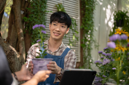 A positive and handsome Asian male florist or flower shop owner handing a potted flower to a customer. small business conceptの写真素材