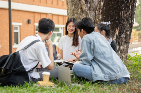 A group of happy young teen Asian students are talking and doing homework while sitting on the grass...