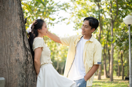 A lovely young Asian couple is flirting in a beautiful green park on a bright day. lovely couple, relationship, boyfriend and girlfriend, husband and wife, bondingの写真素材