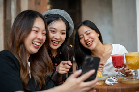 Group of positive and beautiful Asian female friends are enjoying chit chat, gossiping, looking online contents on a smartphone while hanging out at a cafe in the city together.の写真素材