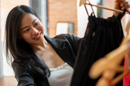 A beautiful Asian female enjoys shopping in the city alone on the weekend, picking cute dresses. Fashion and lifestyle conceptsの写真素材