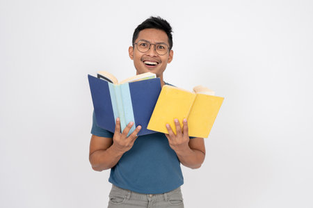 A happy Asian man in casual clothes is posing with books while standing on an isolated white studio background. People and education conceptsの写真素材