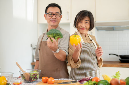Lovely Asian couple are in the kitchen, cooking together, posing with fresh vegetables. Home cooking, domestic life, adult coupleの写真素材