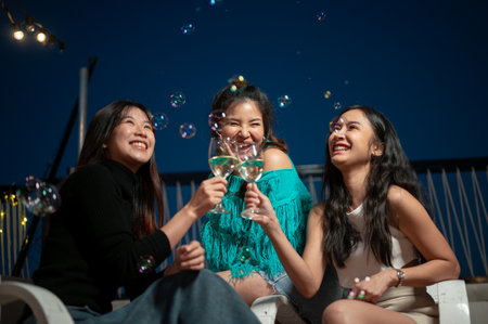 Group of attractive, fun Asian female friends are enjoying drinks and partying on a rooftop bar at night together. champagne toasting, girls night, city life, friendshipの写真素材