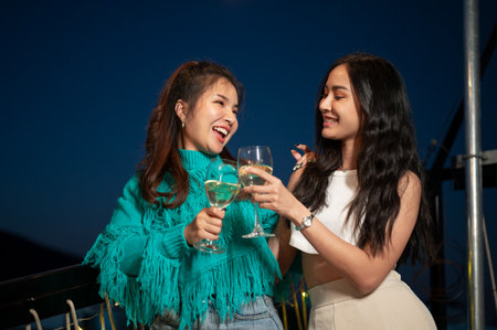 Two attractive, fun Asian female friends are enjoying dancing and drinking champagnes while partying on a rooftop bar together. girls night, city life, friendshipの写真素材