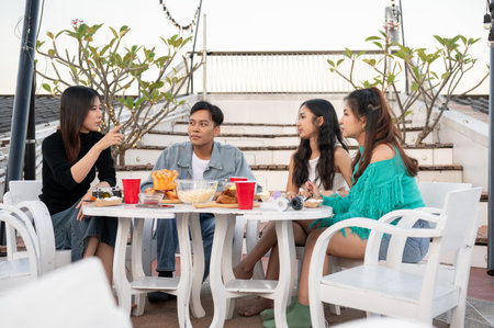 Group of happy young Asian friends partying on a rooftop bar restaurant, having fun, enjoying eating, and talking. celebration and city life conceptsの写真素材
