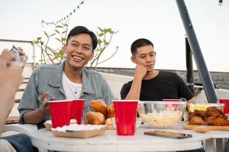 Group of happy young Asian friends partying on a rooftop bar restaurant, having fun, enjoying...