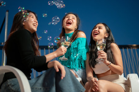 Group of attractive and cheerful Asian girls are enjoying partying on a rooftop bar together and having a fun night out, enjoying talking and drinking champagne. Friendship and celebration conceptsの写真素材