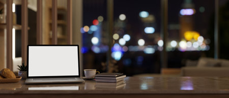 Home workspace at night with a white-screen laptop computer mockup and accessories on tabletop in a modern living room. 3d render, 3d illustrationの写真素材