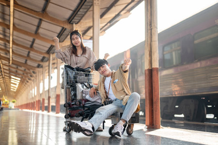 Cheerful young Asian couple are excited for their summer vacation, walking down the platform with a cart, commuting by a train at a railway station.の写真素材