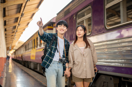 Young happy Asian couple travelers are commuting by train together, walking on a platform at a railway station, and catching the train. People and transportation conceptsの写真素材