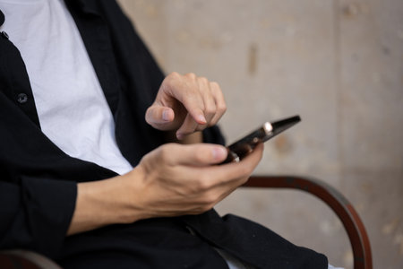 Cropped shot of an Asian man in casual clothes using his smartphone while sitting indoors. modern lifestyle, people, and technology conceptsの写真素材