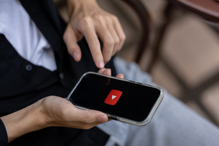 Chiang mai, Thailand - Jan 16 2024: A man using Youtube application on his iPhone while sitting outdoors. Youtube logo on an iPhone screen. close-up imageのeditorial素材